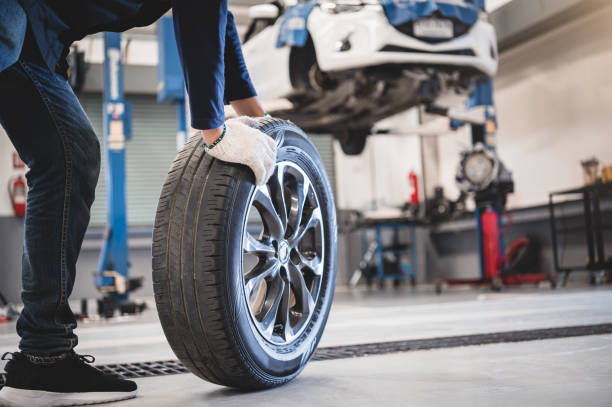 Male mechanic hold and rolling tire at repairing service garage background.