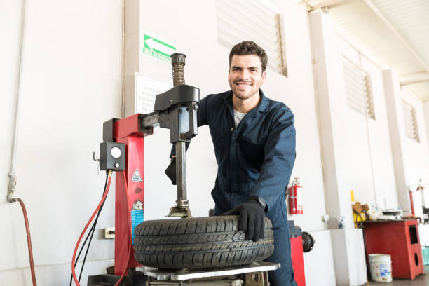 Portrait of smiling mid adult serviceman in uniform using tire changer at garage