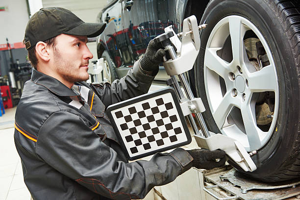car mechanic installing sensor during suspension adjustment and automobile wheel alignment work at repair service station